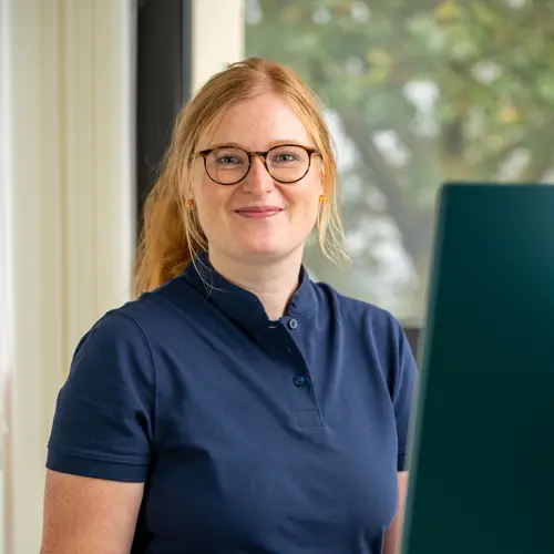 Ein Portraitfoto von Lisa Wolff, die an ihrem Schreibtisch vor einem Monitor sitzt und in die Kamera lächelt.